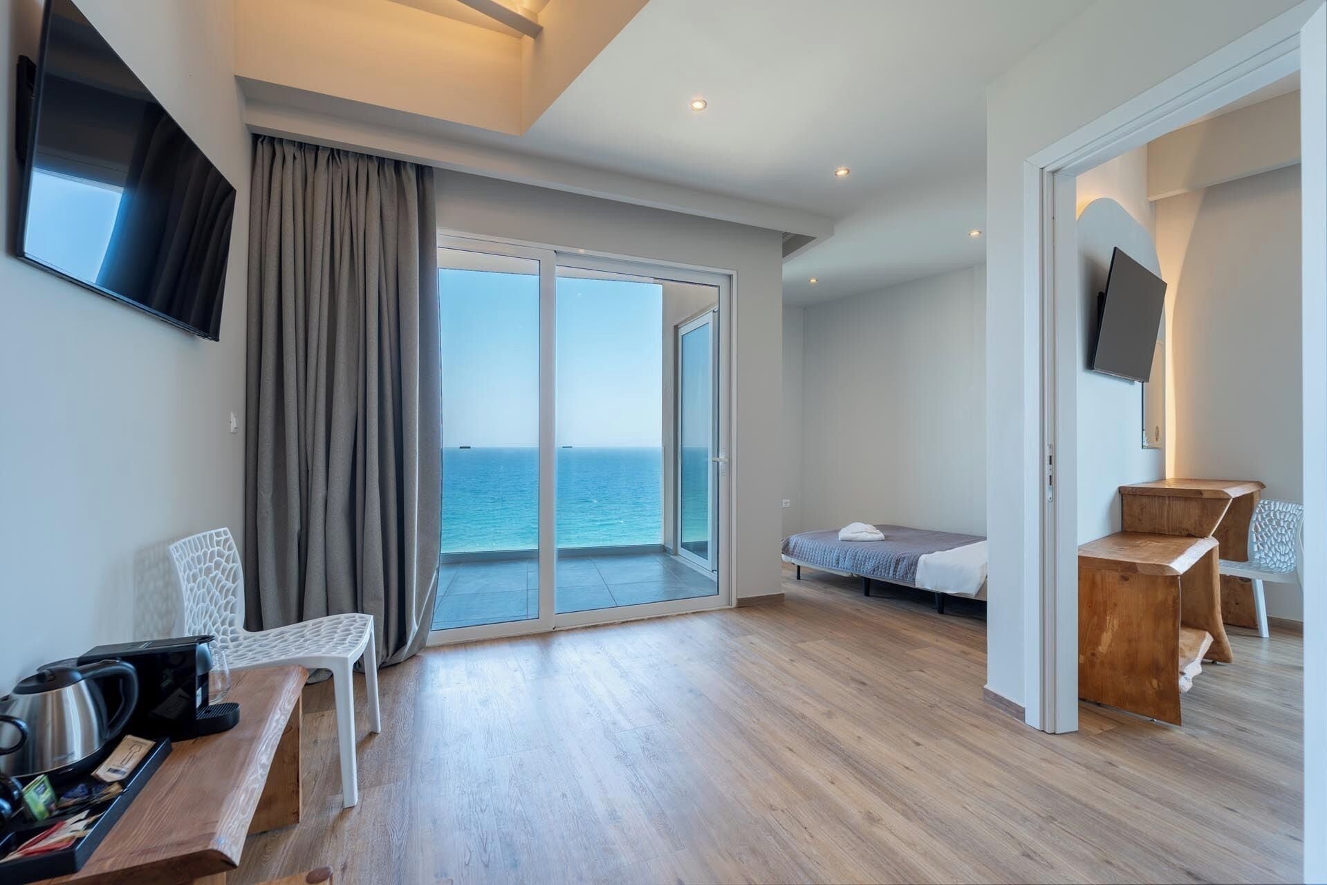 Ein modernes Hotelzimmer mit einer großen Schiebeglasdoor zum Balkon mit Meerblick. Es gibt ein Bett, einen kleinen Schreibtisch und einen Stuhl.