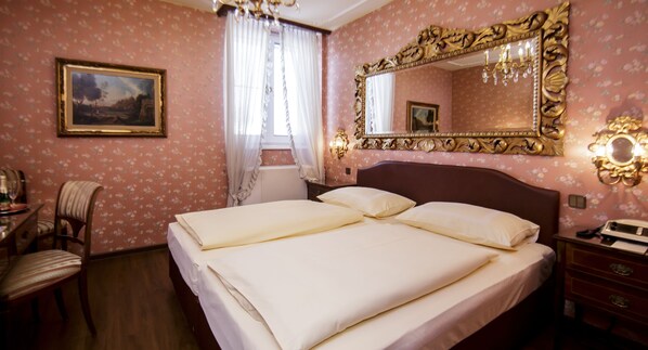 A hotel room with a large bed, a chair, a desk, a dresser, a mirror, and a chandelier.