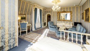 A room with a bed, a blue armchair, a white dresser, a chandelier, and a mirror with a gold frame. - Hotel Palais Porcia (Klagenfurt am Woerthersee)