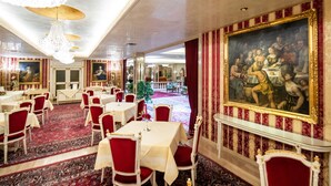 A dining area with red upholstered chairs, white tables, and a large painting on the wall. - Hotel Palais Porcia (Klagenfurt am Woerthersee)