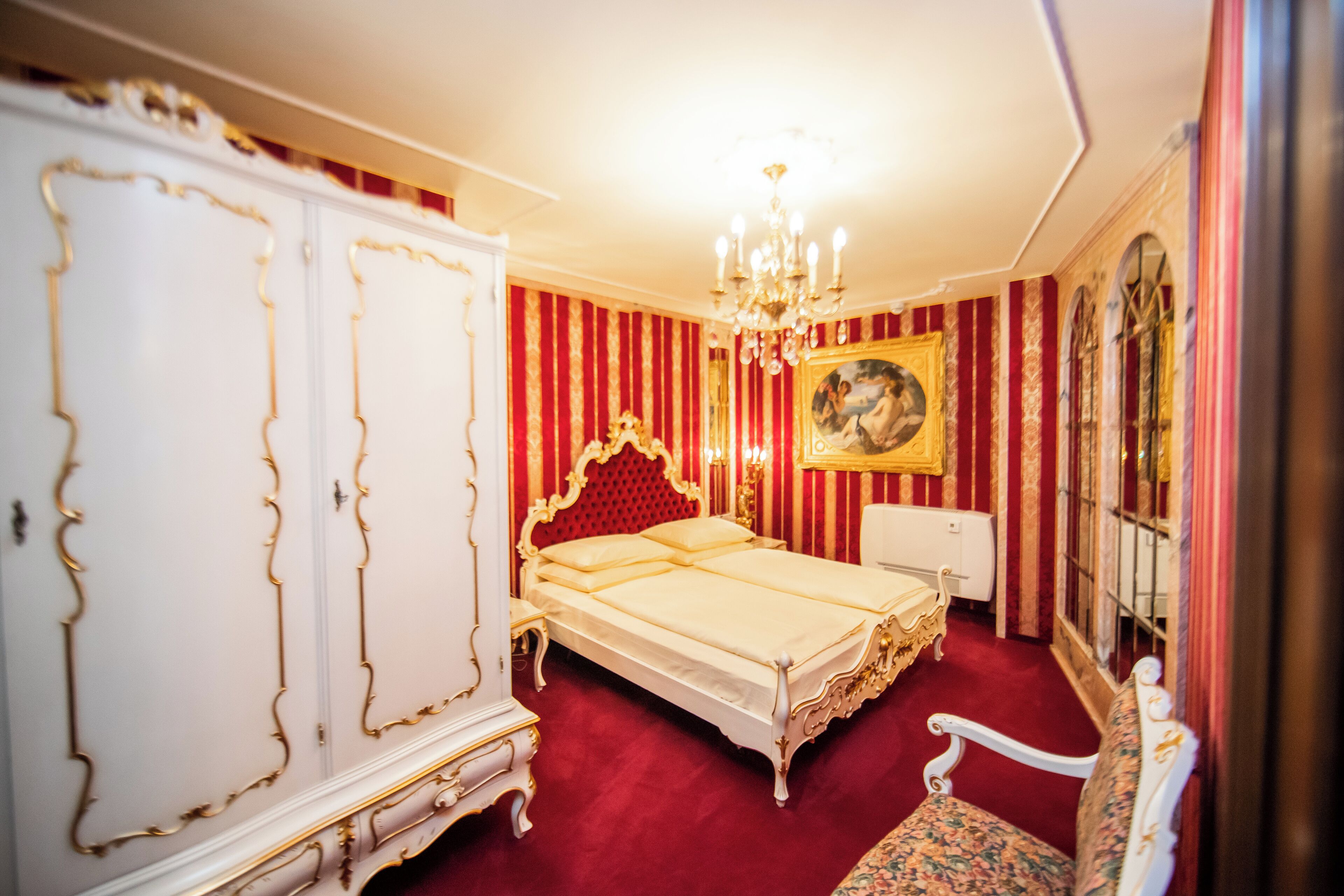 Una habitación con una cama grande, un armario, una silla y un candelabro.