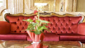A red upholstered sofa with a gold ornate frame, positioned in a room with marble columns and a large mirror reflecting the room's interior.