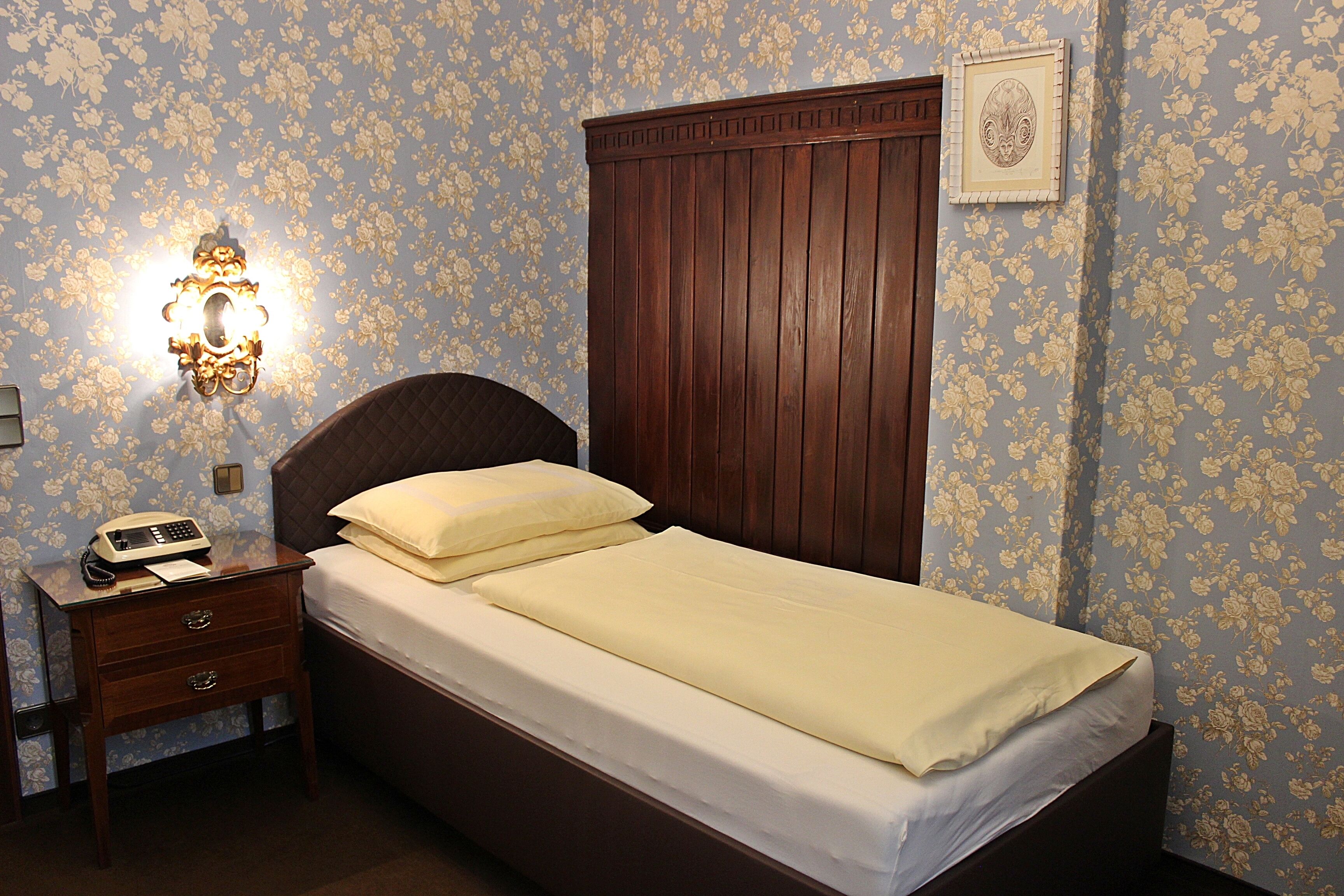 Uma cama bem arrumada com cabeceira de madeira, mesa de cabeceira com telefone e luminária na parede.