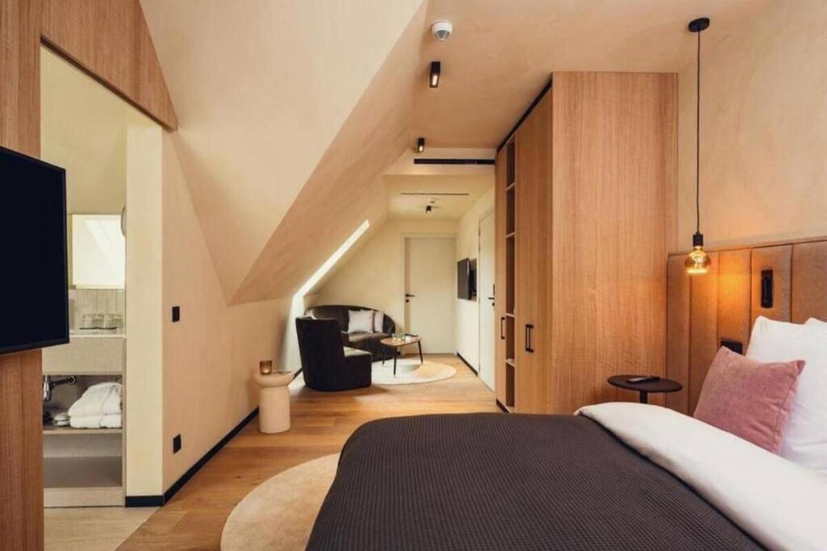 A modern bedroom with a large bed, wooden wardrobe, and a small seating area with a sofa and table.