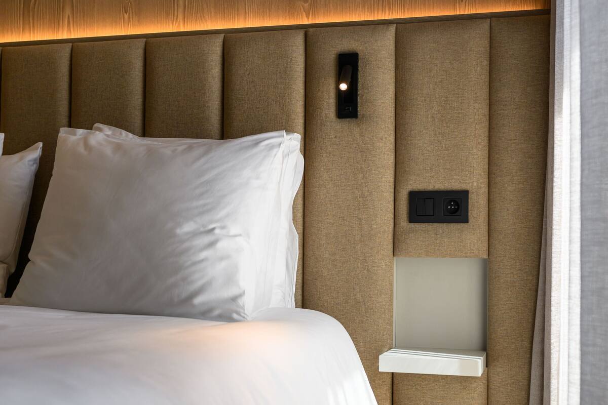 A modern hotel room with a wooden headboard, a bedside table, and a built-in light fixture.
