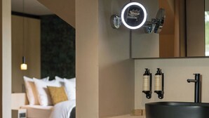 Un baño moderno con un espejo grande, una lámpara redonda y un lavamanos negro. Hay un perchero con toallas dobladas y un secador de pelo en la encimera.
