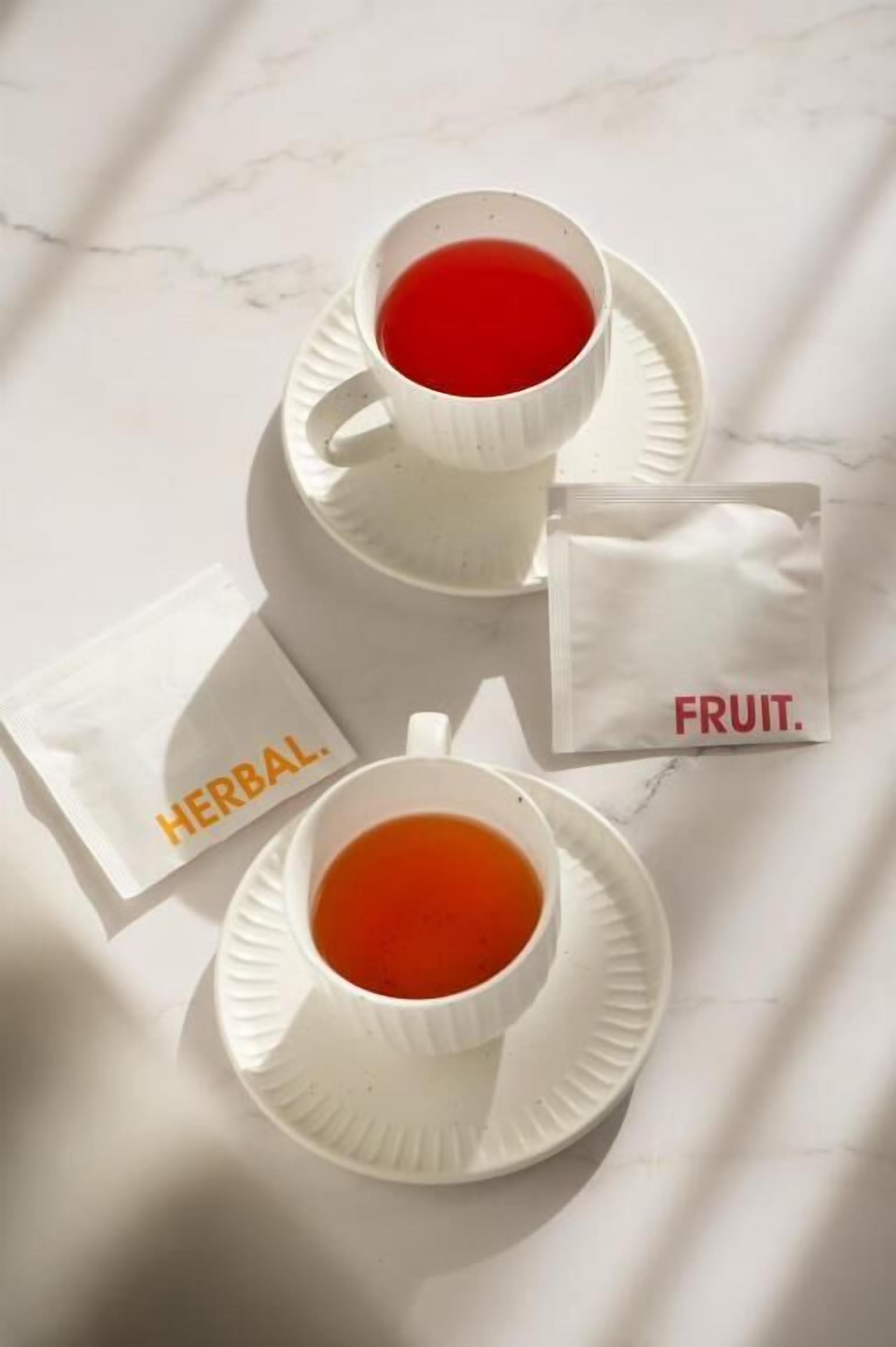 Dos tazas de té sobre platillos blancos con las etiquetas "HERBAL" y "FRUIT".