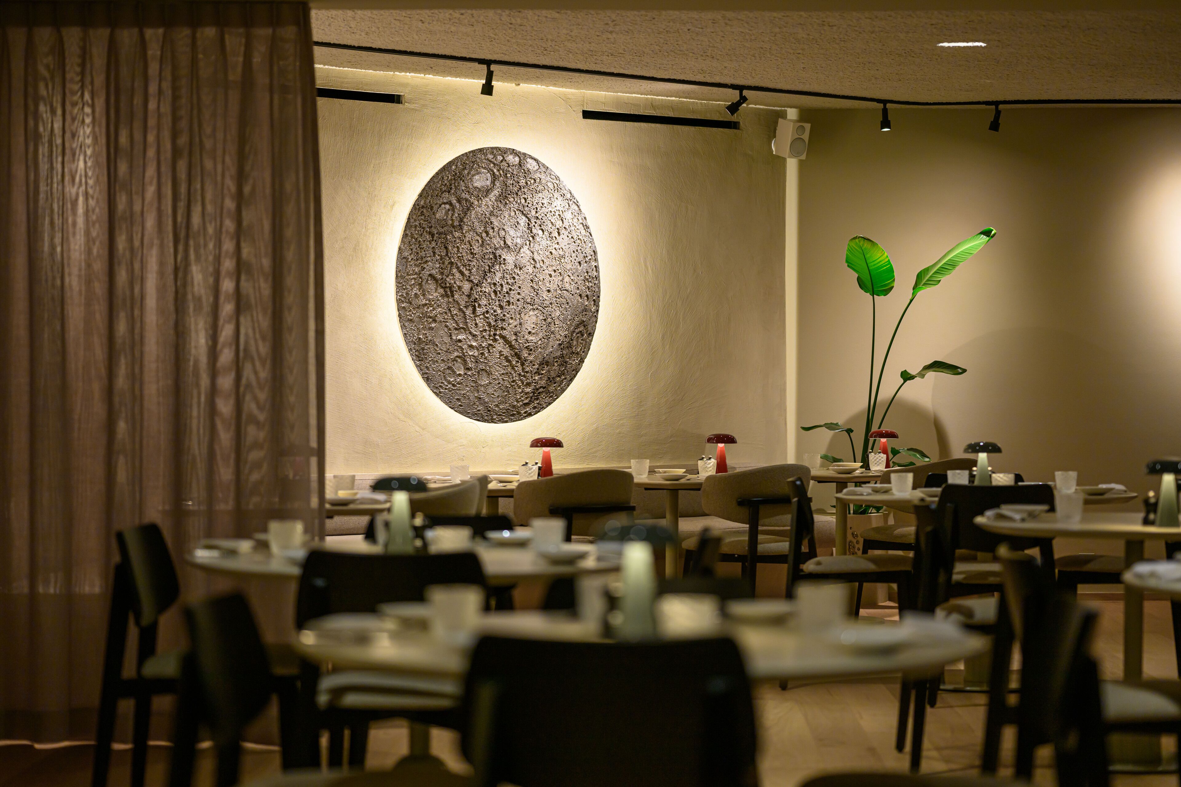 A restaurant interior with round tables, chairs, and a large wall-mounted sculpture.