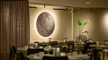 A restaurant interior with round tables, chairs, and a large wall-mounted sculpture.