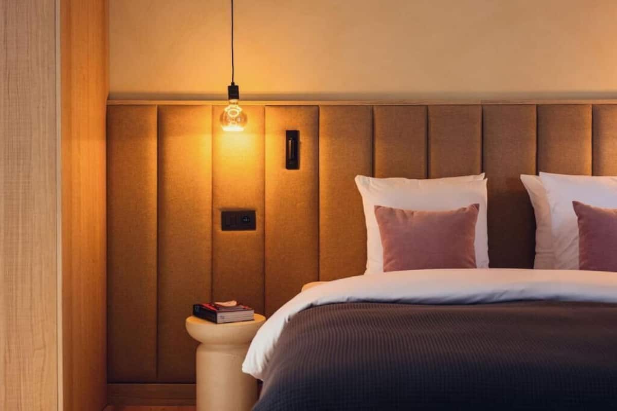 A hotel room with a large bed, a bedside table, and a wall-mounted light fixture.