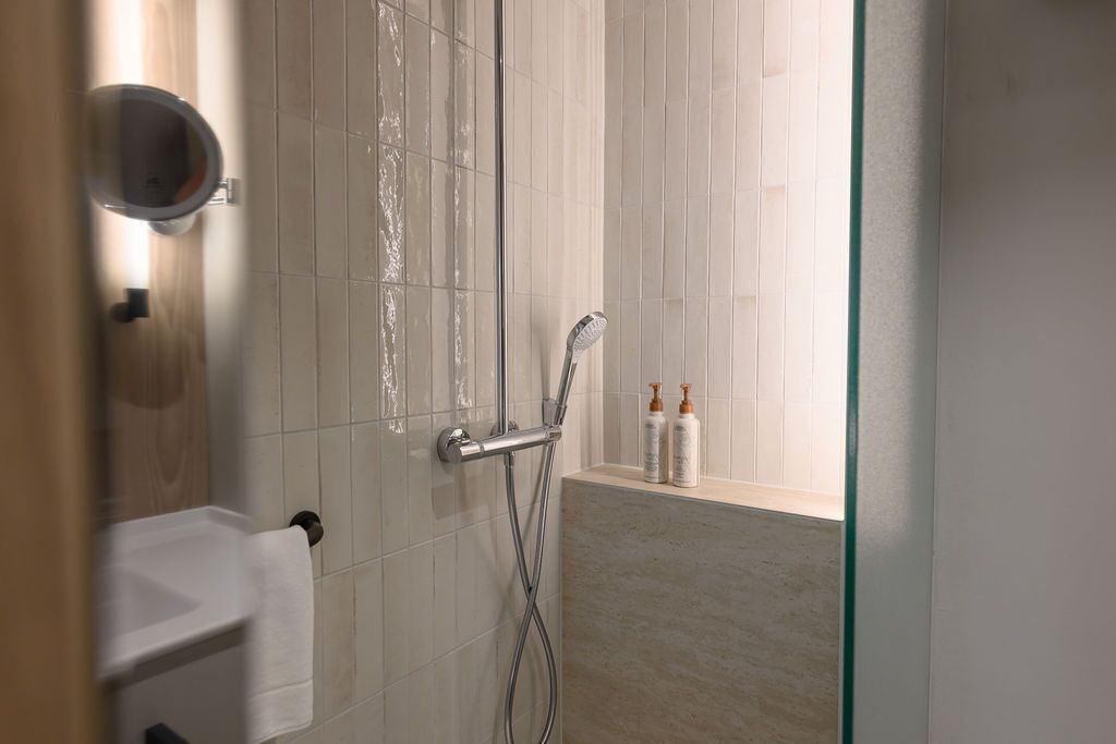 A modern bathroom with a glass shower enclosure, a white sink, and a window sill with toiletries.