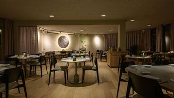 Un comedor amplio con varias mesas y sillas, una mesa redonda central y un elemento decorativo en la pared.