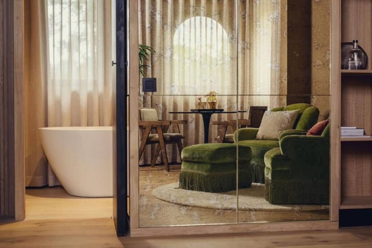 A modern bathroom with a freestanding bathtub, a green upholstered sofa, and a round table with chairs.