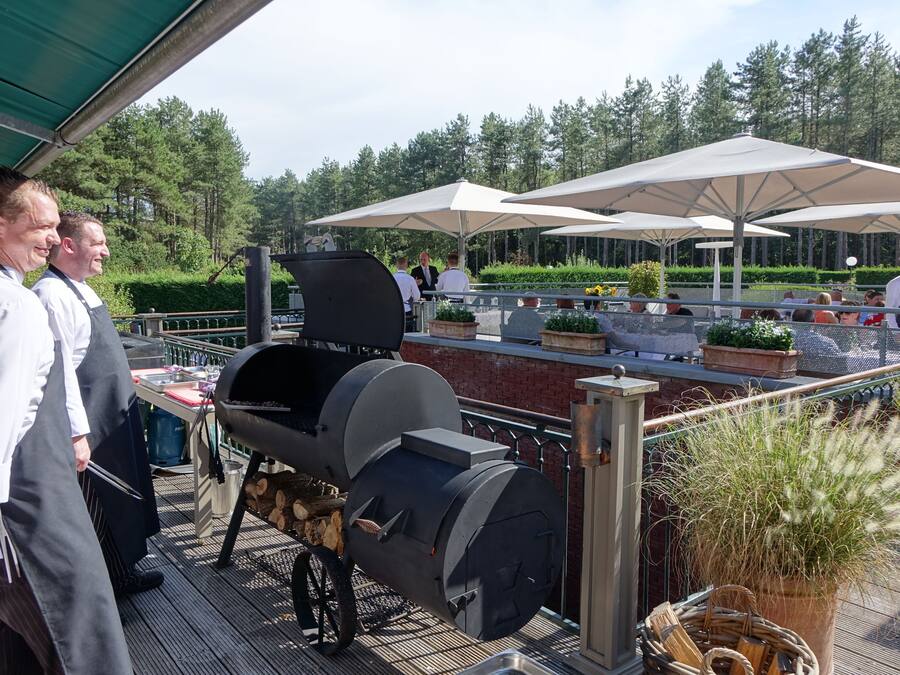 An outdoor dining area with a barbecue grill, umbrellas, and potted plants.
