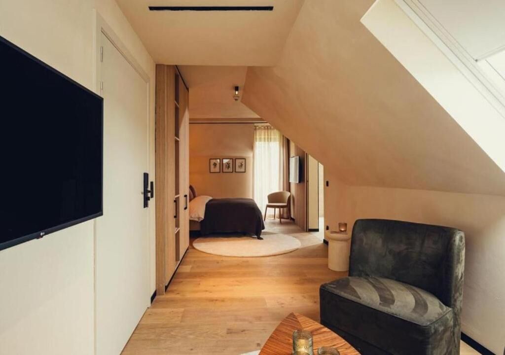 A narrow hallway leading to a bedroom with a bed, a chair, and a small table.