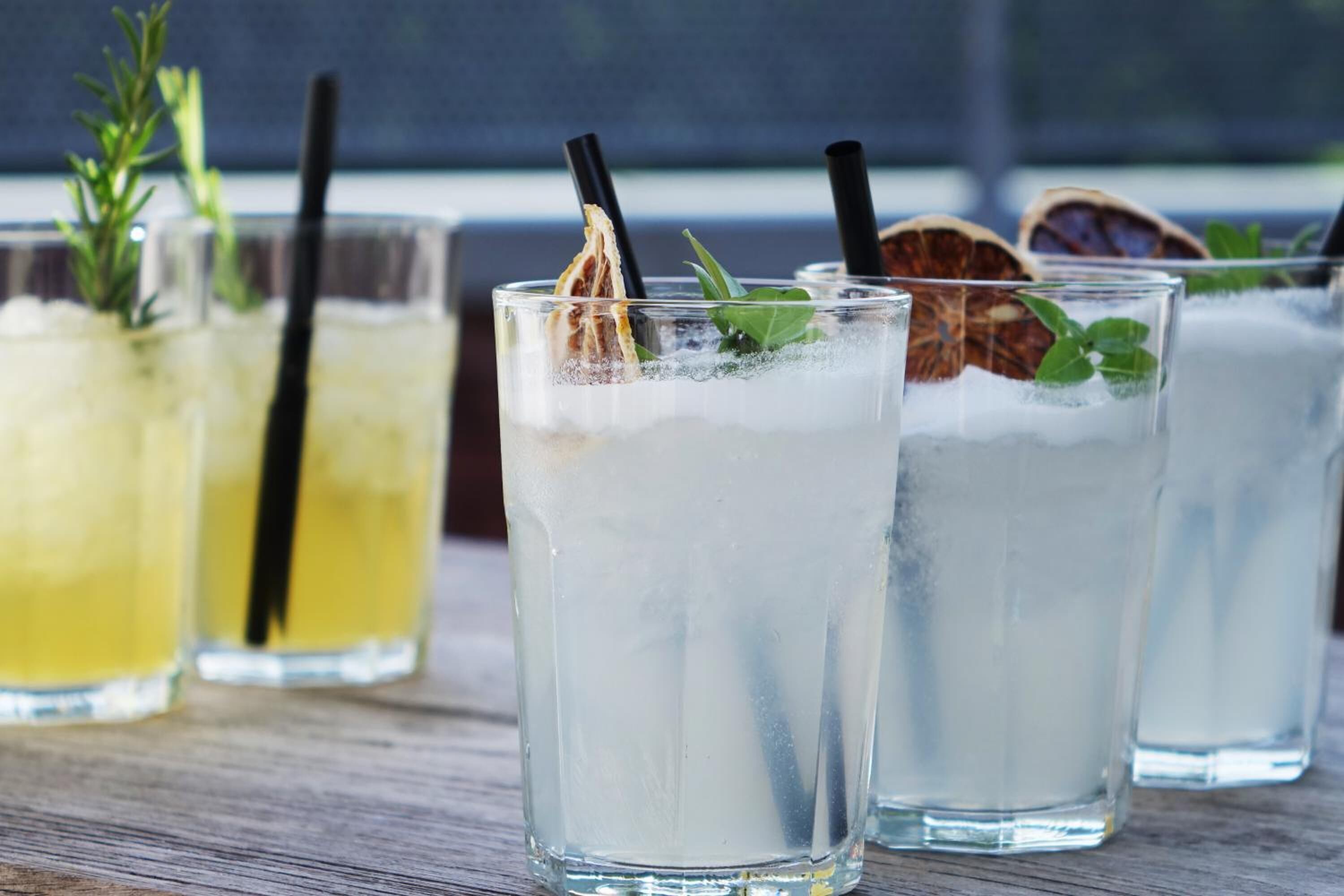 Trois verres de boissons glacées, avec des pailles et des décorations, posés sur une surface en bois.