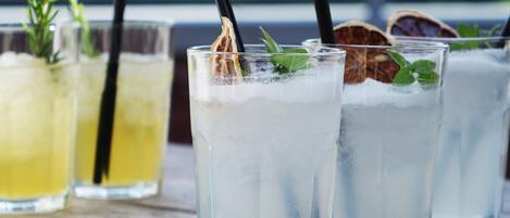 Three glasses of iced beverages with straws and garnishes on a wooden surface.