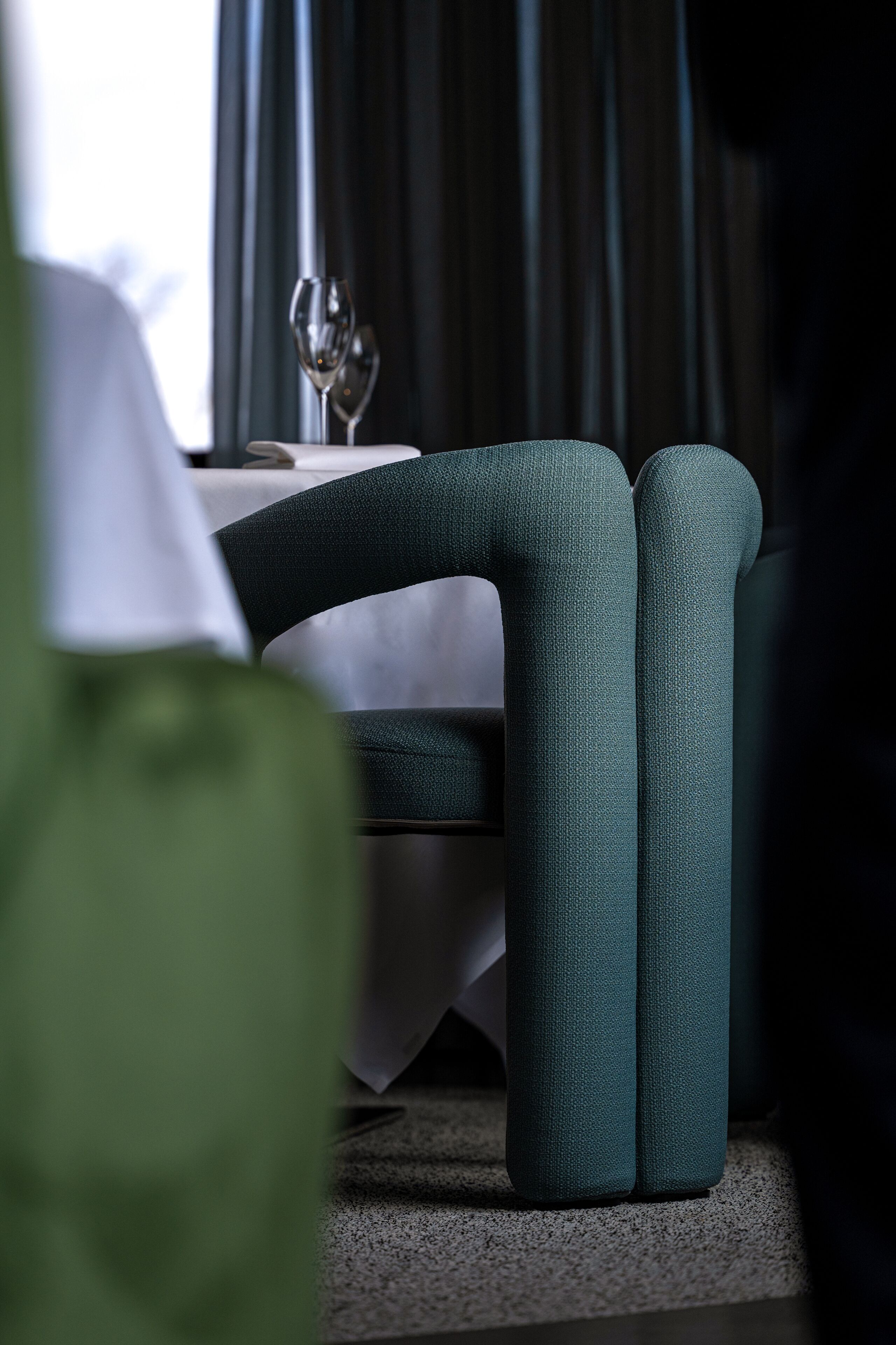 Un comedor con una mesa dispuesta para dos, una copa de vino y una silla con tapicería texturizada.