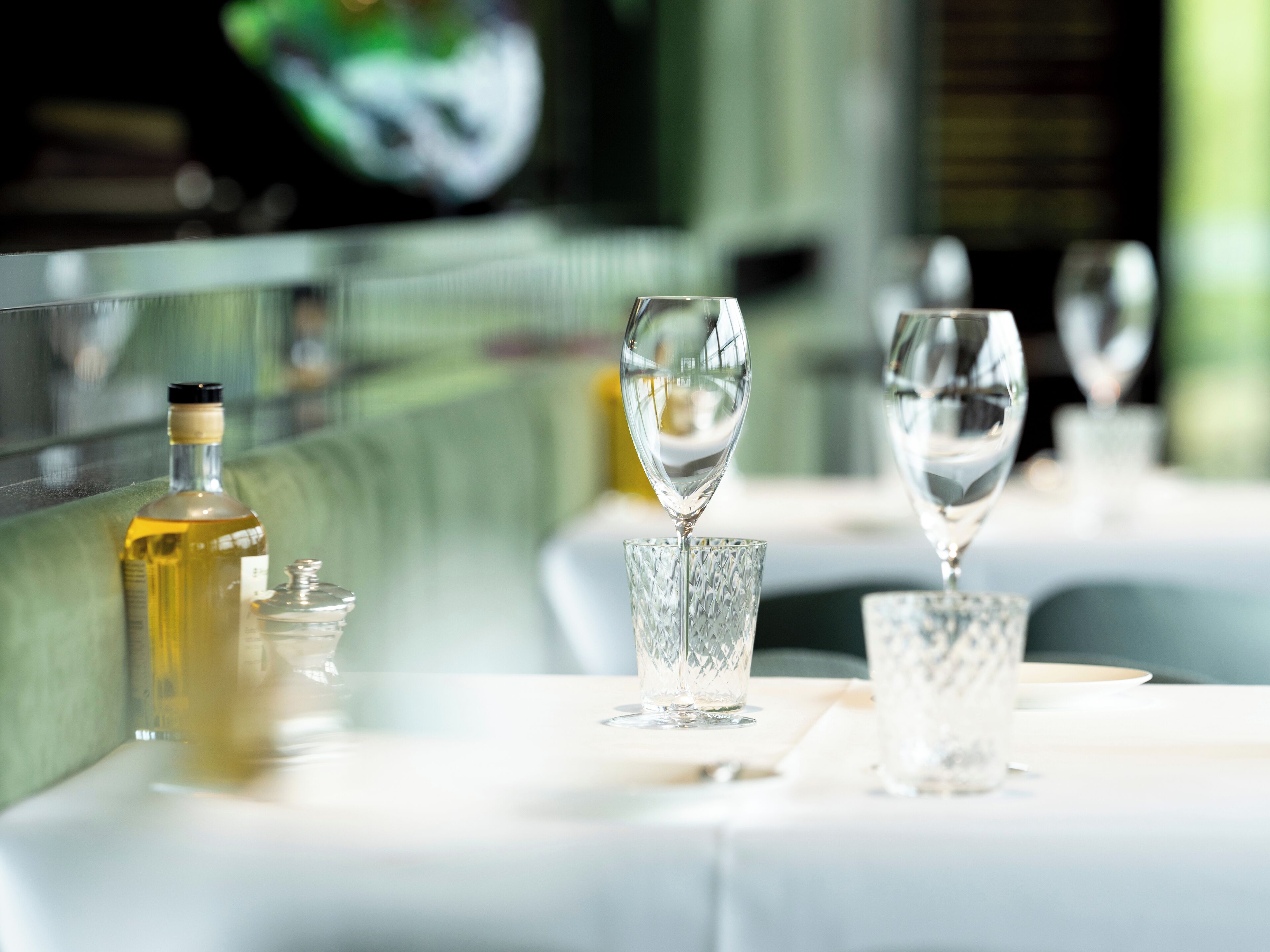 Une table à manger avec une bouteille d’huile d’olive, deux verres en cristal et un petit récipient en verre.