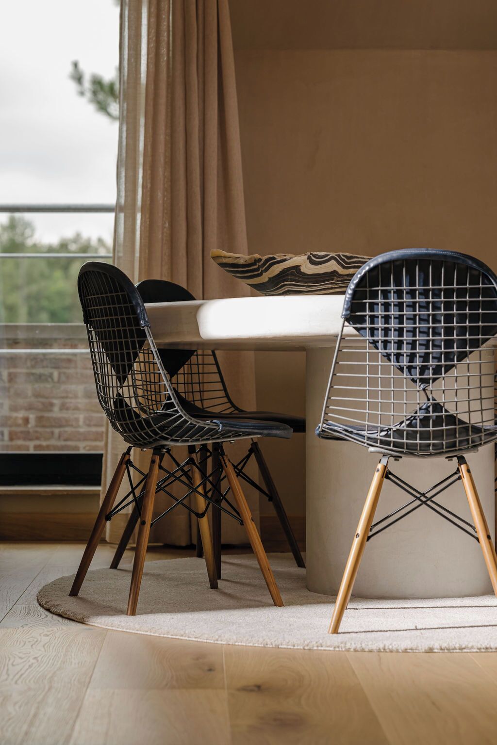 Two wireframe chairs with wooden legs, a white table, and a beige cushion with a striped pattern.