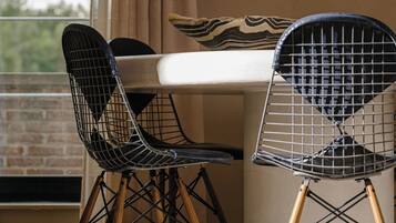 Two wireframe chairs with wooden legs, a white table, and a beige cushion with a striped pattern.