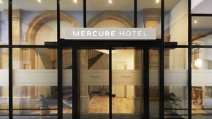 The entrance of the Mercure Hotel with a modern glass facade, a sign above the doors, and a view of the interior including a staircase and a reception area. - Mercure Grand Hotel Metz Centre Cathédrale (Metz)