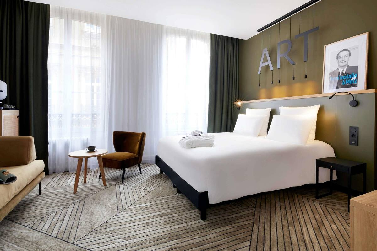 A hotel room with a bed, a chair, a small table, and a sofa.