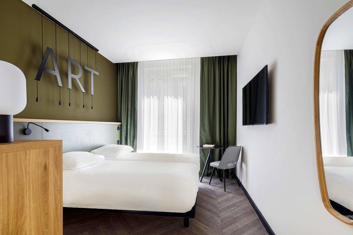 A hotel room with a bed, a desk, a chair, a TV, and a large mirror.