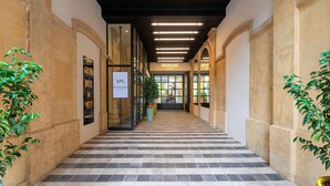 A hotel corridor with checkered flooring, glass doors, and potted plants. - Mercure Grand Hotel Metz Centre Cathédrale (Metz)