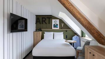 Une chambre moderne avec un plafond en pente, un lit, un téléviseur fixé au mur et une petite table avec une chaise.