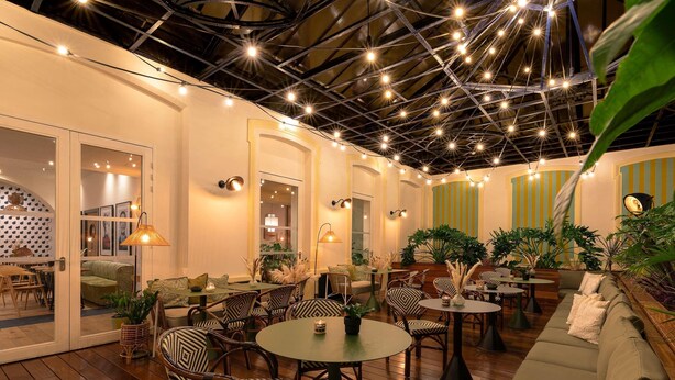 An indoor patio area with wooden flooring, round tables, wicker chairs, and a green sofa. - Mercure Grand Hotel Metz Centre Cathédrale (Metz)