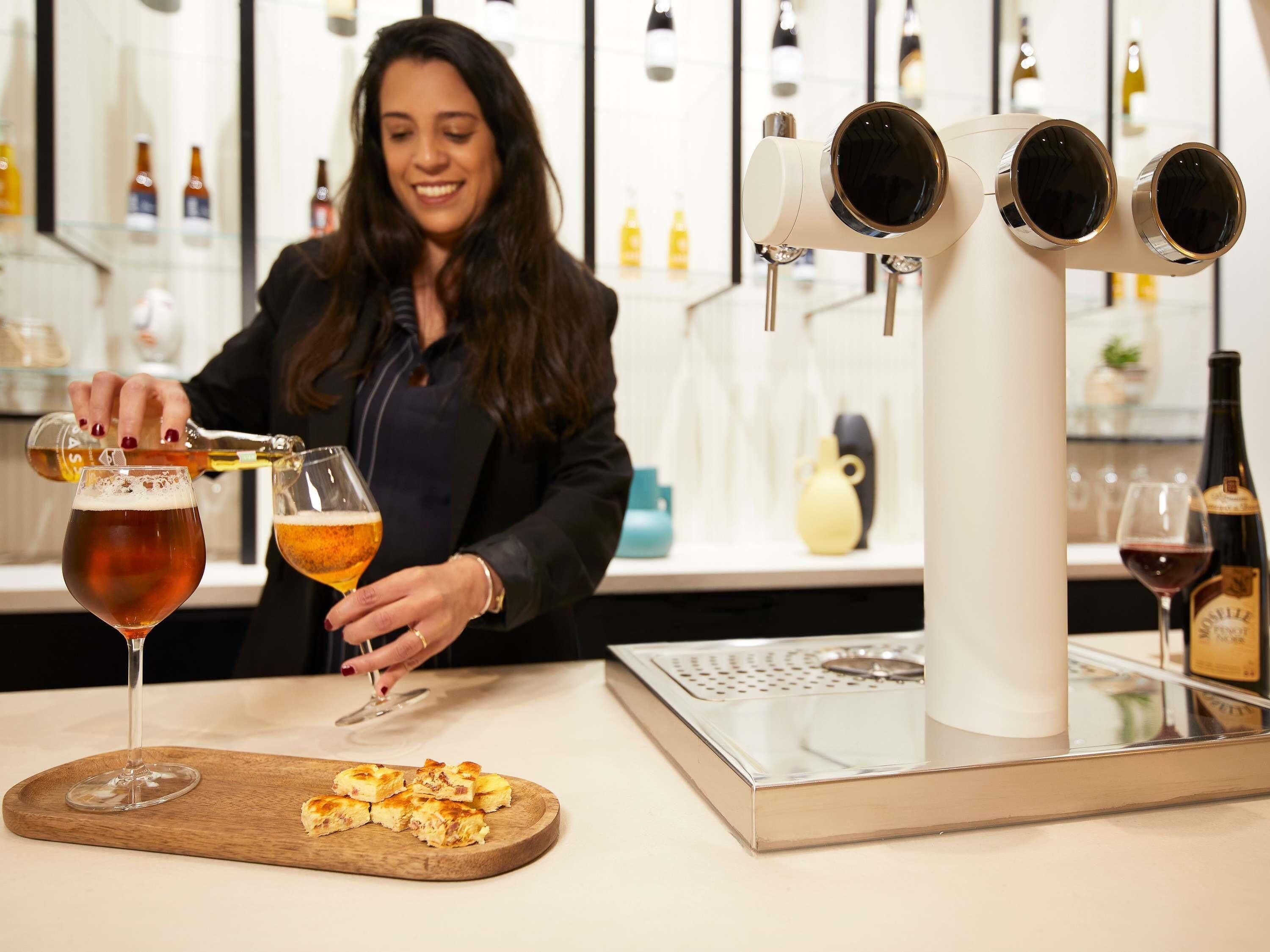 Un bar con una persona sirviendo cerveza en vasos, una bandeja de comida y una botella de vino.