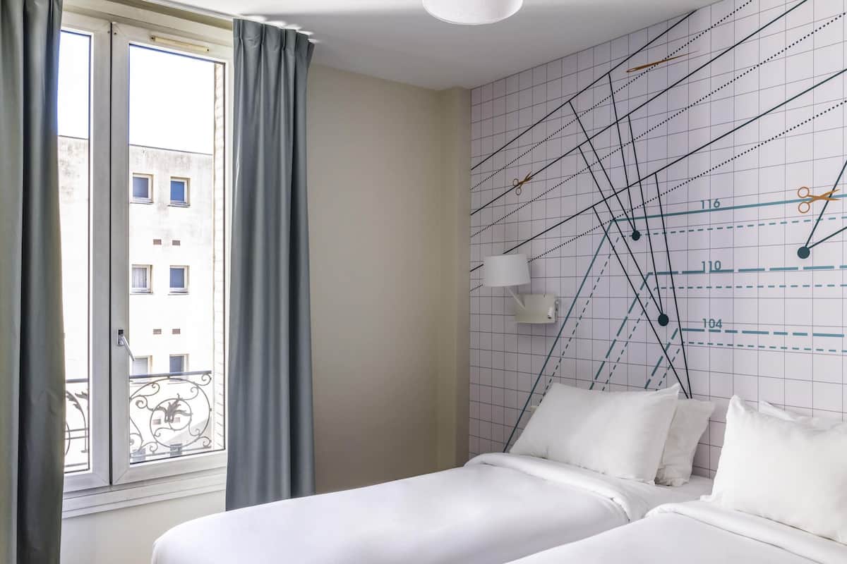 A hotel room with two beds, a window with curtains, and a wall with a grid pattern and lines.