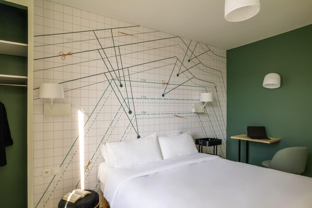 A bedroom with a bed, bedside tables, a chair, a wardrobe, and a wall with a geometric pattern.