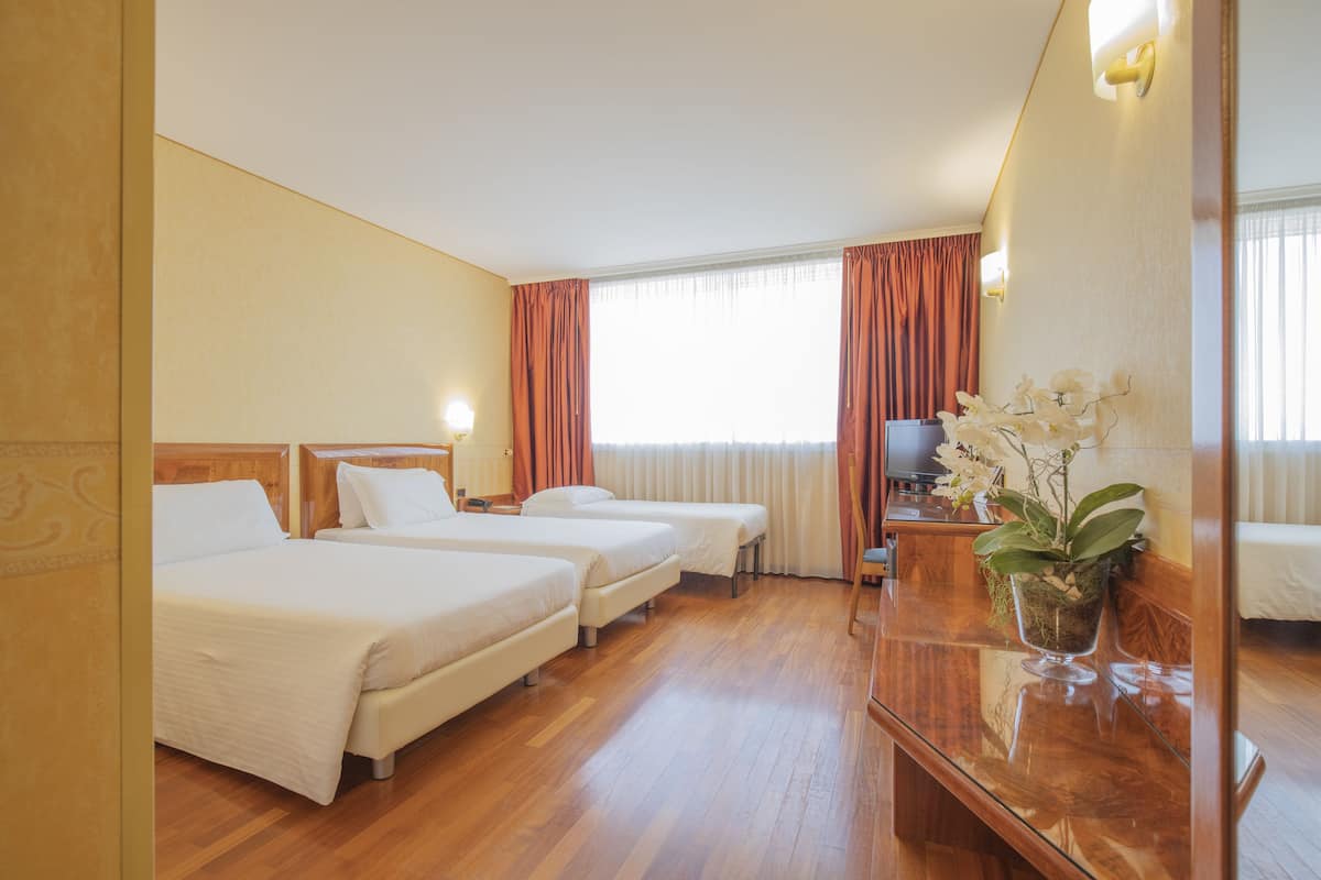 A hotel room with three beds, wooden flooring, a large mirror, and a potted orchid.