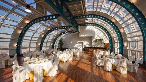 Un salón amplio con techos altos y ventanas grandes, mesas dispuestas para un evento formal.