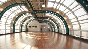 Un interior espacioso con techo alto y ventanas grandes, que presenta piso de madera y elementos estructurales verdes.