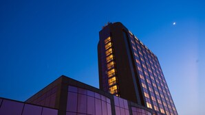 Un edificio moderno con fachada de vidrio y una estructura alta con ventanas iluminadas.