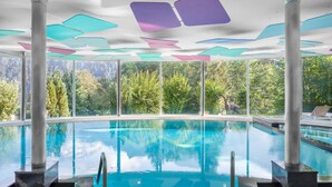 Una piscina interior con paredes de vidrio transparente, rodeada de grandes ventanales que ofrecen vistas a árboles y zona boscosa.