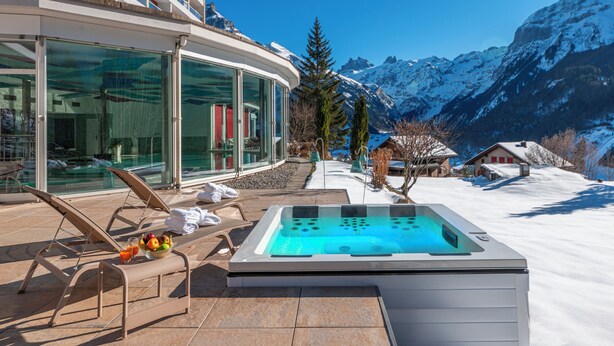 Un jacuzzi con vista a la montaña, una sala con paredes de vidrio y vistas, y un paisaje cubierto de nieve.