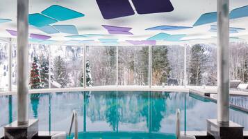 An indoor swimming pool with a view of snow-covered trees and a Christmas tree.