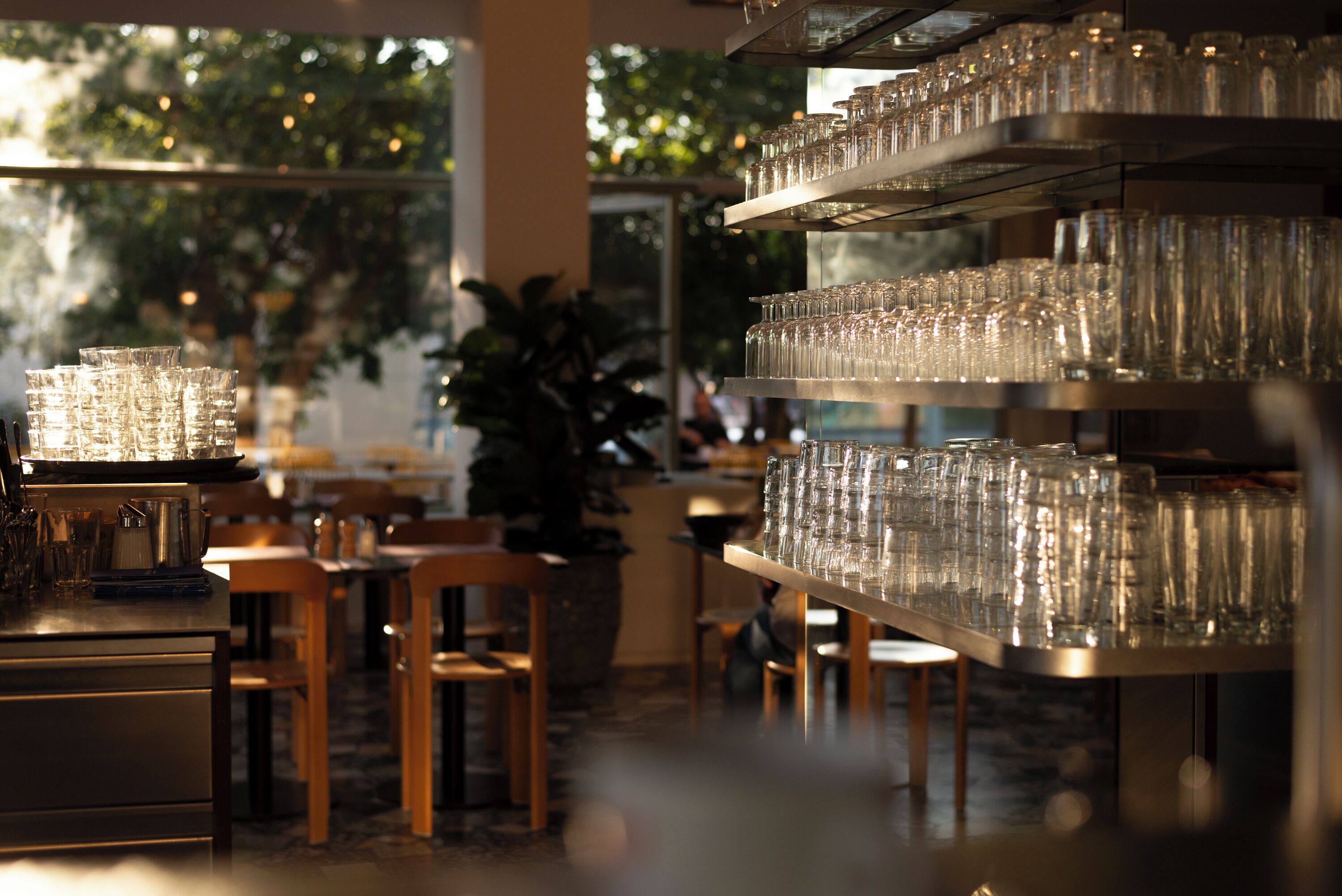 L’intérieur d’un restaurant, avec de nombreuses tables, des chaises et des étagères remplies de verres transparents.