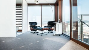 Espaço de escritório moderno com duas cadeiras de escritório pretas, uma mesa branca e uma janela grande com vista para a cidade.