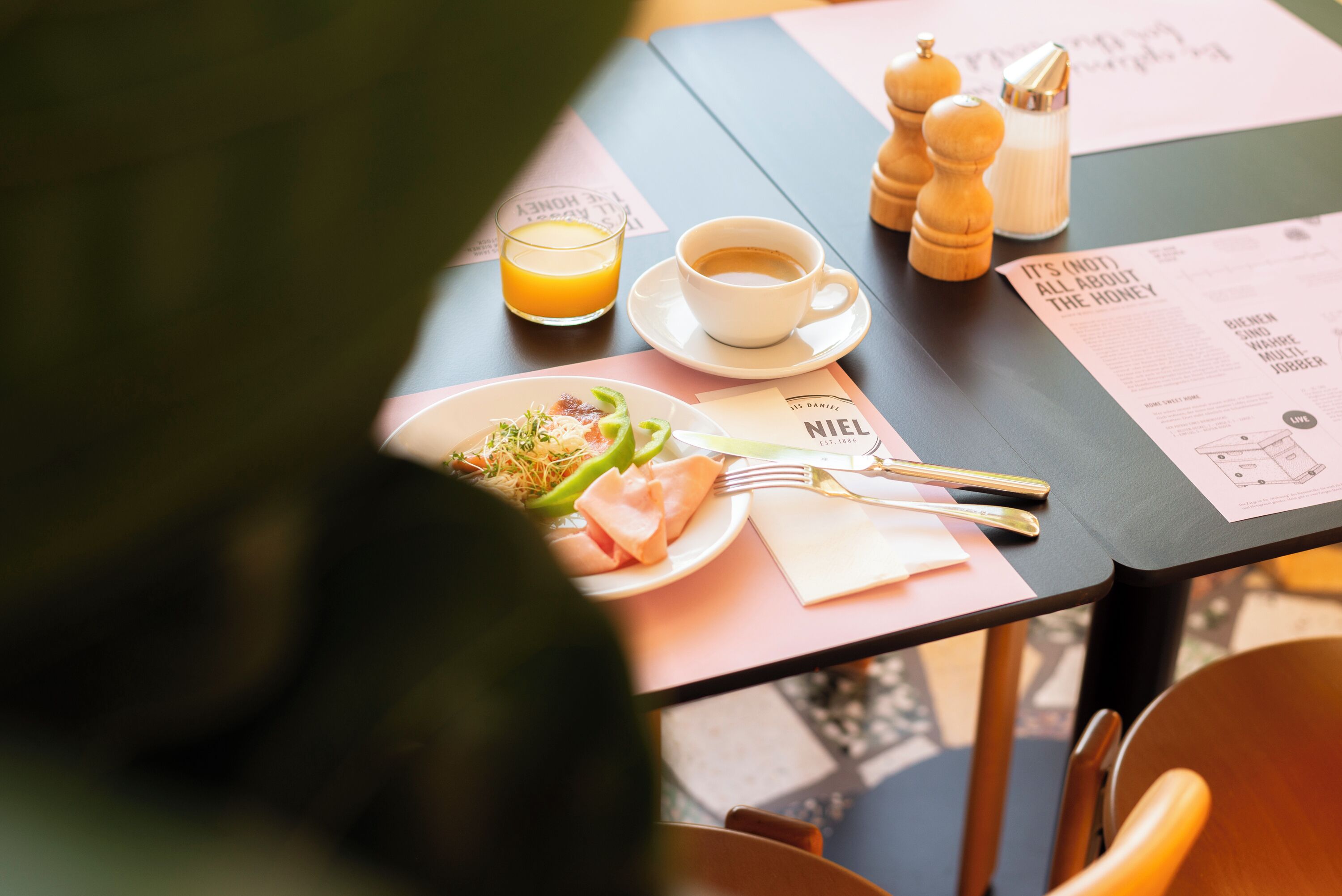 A table with a menu, a cup of coffee, a glass of orange juice, and a plate of food.
