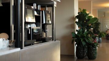 A modern kitchen with a built-in coffee machine, stainless steel appliances, and potted plants.