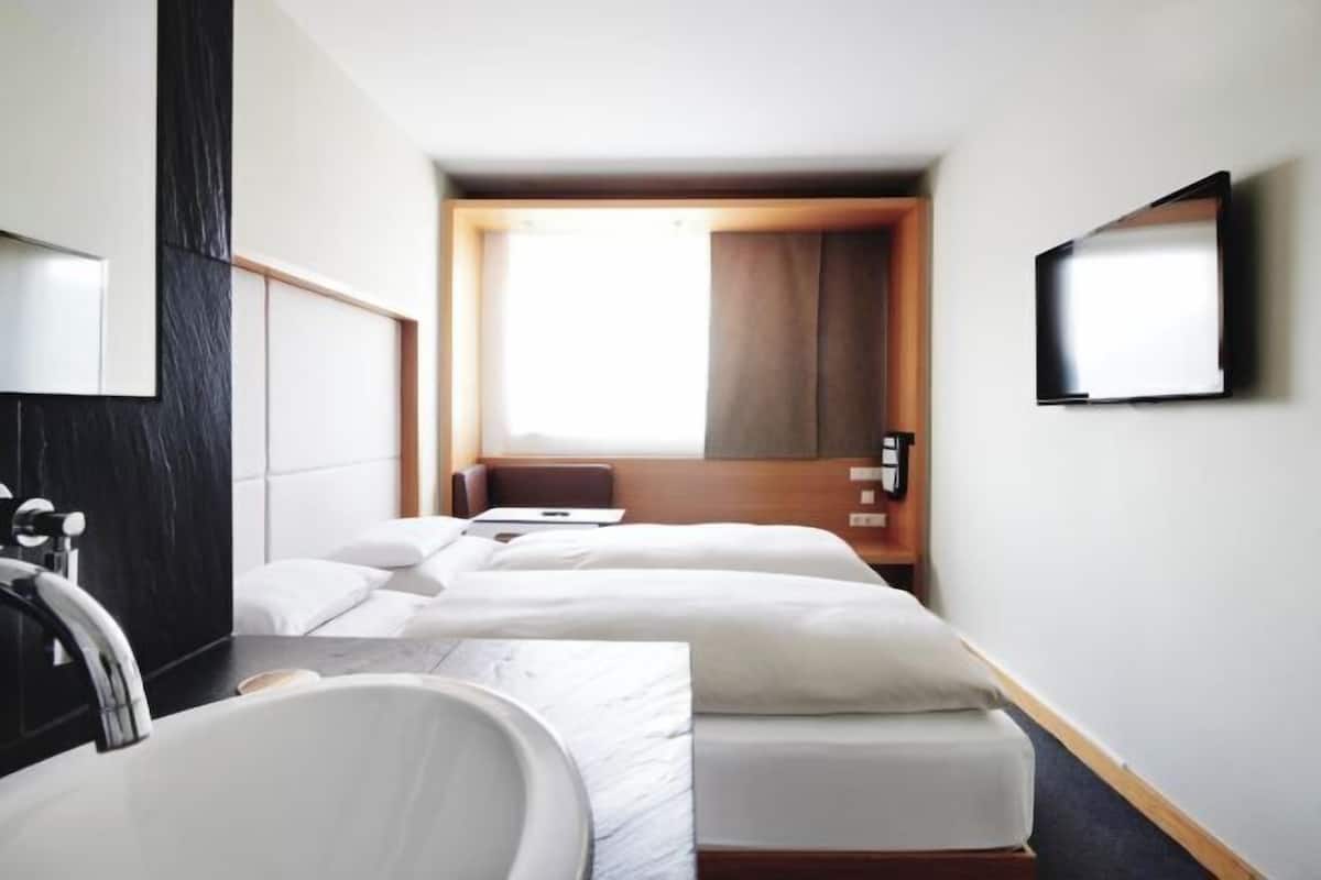 A hotel room with a large bed, a bedside table, a mirror, a TV, and a bathroom with a sink and toilet.