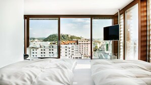Quarto de hotel com uma janela grande, uma cama e uma televisão.