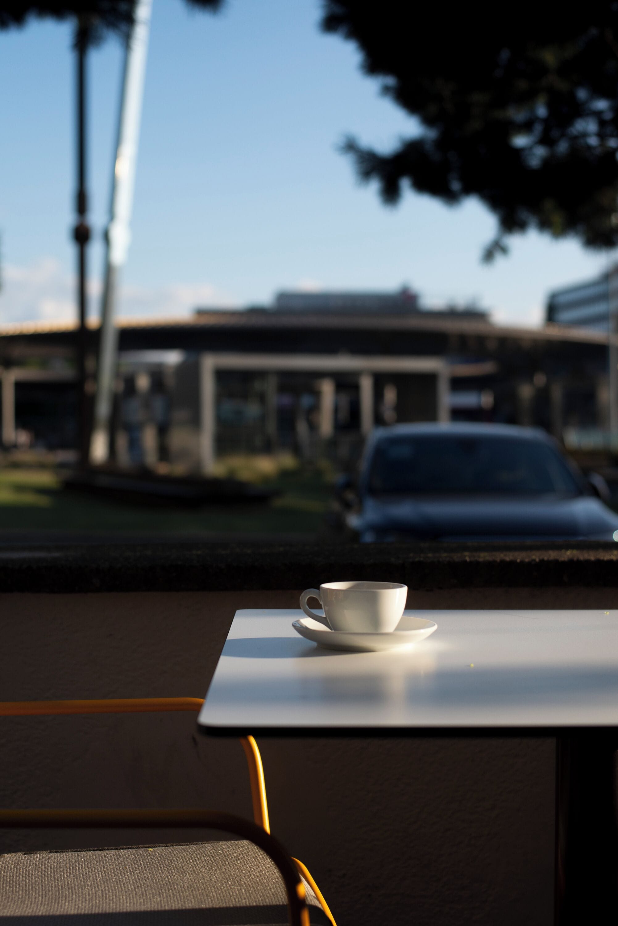 Une tasse posée sur une table, avec en arrière-plan un bâtiment et une voiture.
