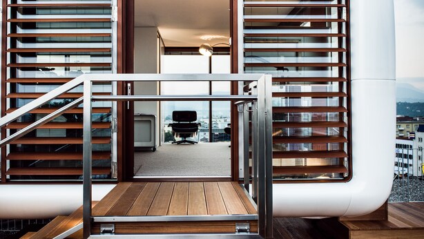 Interior moderno com escada que leva a uma varanda, vista da cidade e um vislumbre do espaço interno.