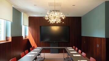 A conference room with a large flat-screen TV, a chandelier, and red chairs.
